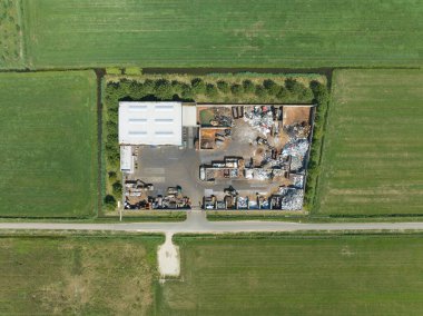 Metal geri dönüşüm şirketine tepeden bakan drone görüntüsü. Metal ve kazıcı yığınları metali işliyor.