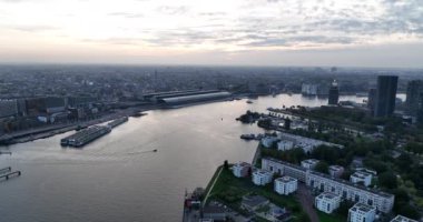 Gün batımından hemen önce Amsterdam 'ın insansız hava aracı görüntüsü, Lj nehri, feribot, su üzerinde ulaşım. Tren istasyonu, merkez işaretleri ve binalar. Turizm merkezi, Amsterdam,