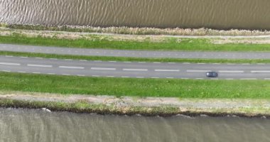Suyla çevrili asfalt bir yolda havadan tepeden aşağıya dron görüntüsü.