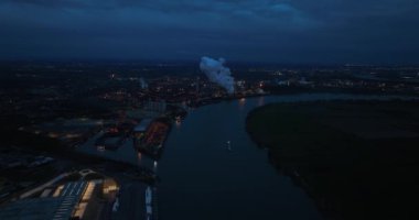 Almanya 'nın ağır sanayileşmiş bir bölgesinde gece vakti Ren Nehri üzerinde kola fabrikası uçuyor. Kuş bakışı.