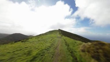 FPV, lagoa do fogo, krater gölü çevresindeki yeşil tepelerin üzerinden uçuyor. Otlaklar sisli bulutlar uçuşuyor.