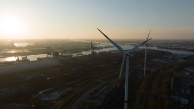 Amsterdam limanında rüzgar türbini, ağır sanayi, su üzerinde ulaşım ve yenilenebilir enerji sergiliyor. Gün batımında hava aracı fotoğrafı.