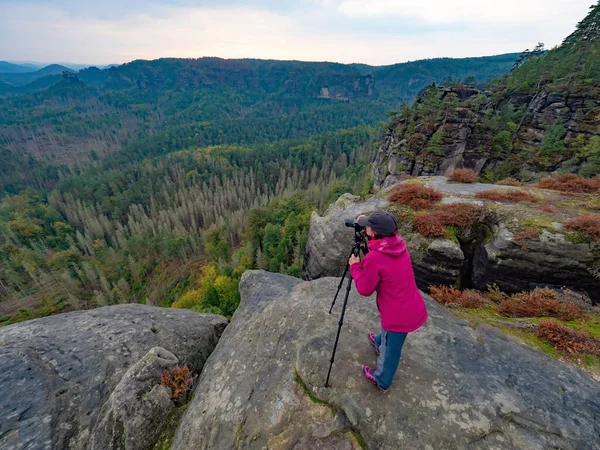 Woman photographer is taking pictures with camera in morning hills. Nature landscape photographer with photo equipment on rock