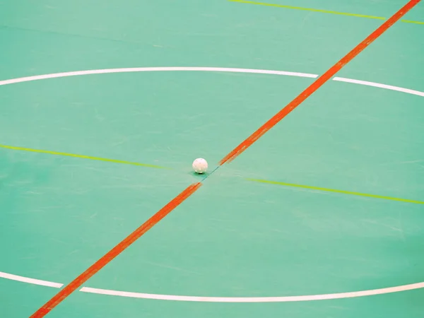 Bully of floor-ball court. White ball in middle on floor of sports hall with colorful marking lines.