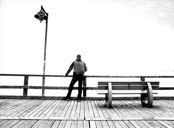 Pensive guy in trekking suit  on a wooden pier above the water.  Tourist at dusk on the docks bridge. Black and white dashed retro sketch.