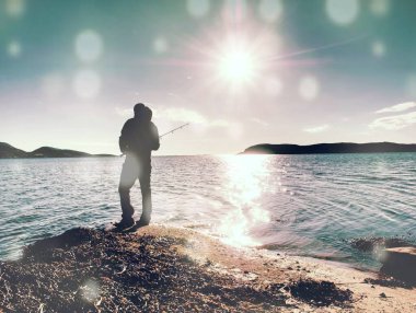 The active man is fishing on sea from the rocky coast. Sunny day