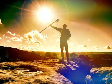 Man raised arm with trekking stick. Tourist hiking mountain trail, walking on sandstone rocky hill, wearing backpack