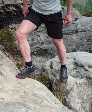 Dağ zirvesinde siyah kırmızı yürüyüş botlarıyla yürüyüş yapan bacakların ayrıntıları. Ayaklar yürüyüş ayakkabılarında ve bacaklar arka planda açık renk pantolonlar