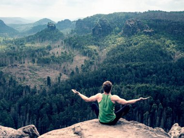 Yoga pozuyla dağın tepesinde tek başına oturan adam. Nefes kesici bir manzarayla kenarda yoga yap. 