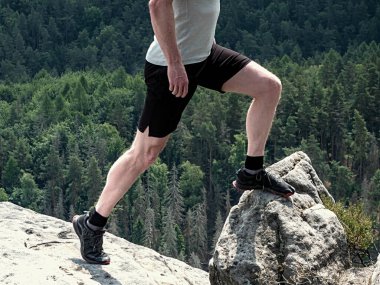 Uzun bacaklı yürüyüş ayakkabıları zirvede. Kum taşı kayalıklarında yürüyüş, tepelik arazide arka planda mavi sisli bulut. 