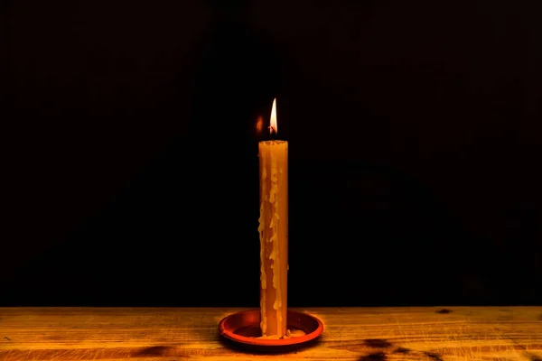 Candle light on the wooden table in the dark night.Single burning candle. Light of flame and flowing candle wax, dark background.Copy space.