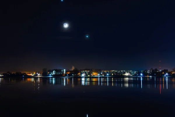 stock image Telsiai town,water,moon night lake in Lithuania. Nice view winter of colorful houses on coast of frozen Lake.Nice winter night.Town colorful light reflections on water.Long exposure.