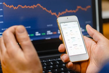 Ticaret ve finans kavramı. İşadamı akıllı telefonu ve dizüstü bilgisayarı ile borsayı kontrol ediyor. Mali borsa alım satım işlemlerini analiz ediyor. Telsiai, Litvanya. 03-30-2023
