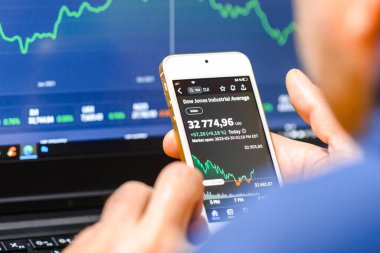 İşadamı akıllı telefonu ve dizüstü bilgisayarı ile borsayı kontrol ediyor. Borsa alım satım verilerini analiz ediyor. Ticaret ve finans konsepti. Telsiai, Litvanya. 03-30-2023