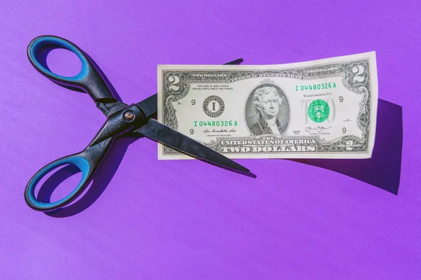 Financial concept.scissors cut money on purple background.Concept of spending money,scissors cut money of USA.