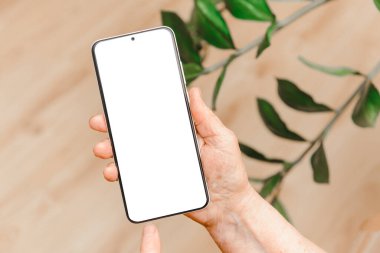 Üst düzey kadın elinde akıllı bir telefon, boş bir ekran, evde sosyal medya uygulaması reklamları için boş bir ekran. Kadın el yazısı. Mobil uygulamalar teknolojisi kavramı. Reklam için boş alan.