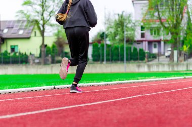 Spor giyimli bir genç kız yaz günü stadyumda koşu pistinde koşuyor. Sağlıklı yaşam tarzı..