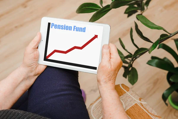 Old woman looking at pension fund growth chart on tablet computer at home.