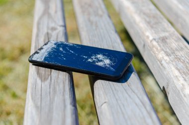 Park 'ta ahşap bir bankta kaza yapmış bir telefon. Parkta kırılmış bir akıllı telefon. Yakın plan..