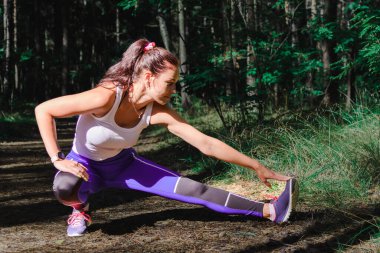 Genç bir kadın yaz günü dışarı çıkmadan önce esneme hareketleri yapıyor. Egzersiz ve Yaşam Tarzı konsepti. Mutlu bir hayat ve sağlık hizmeti teması. Doğa ve Açık hava teması.