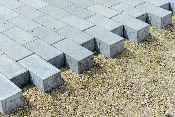 Мостовые и тротуарные плиты, лежащие на подготовленной поверхности, с кубиками плитки на заднем плане. Укладка тротуарной плитки в пешеходной зоне города..