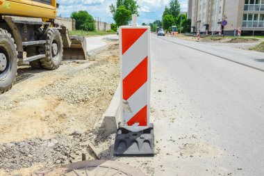 Şehir caddesinde yol işliyor. Kazıcı kovası eski kaldırımı toplayıp bir çöp kamyonuna yüklüyor..