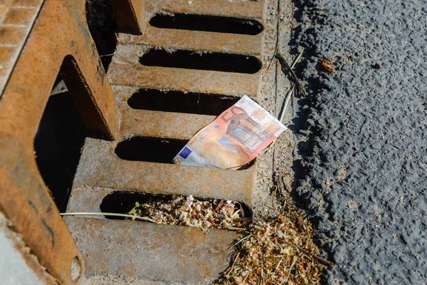 Eu 50 euro banknote down the street storm drain. Concept of senseless waste of money, loss, useless waste.
