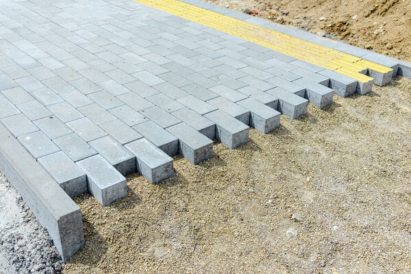 Мостовые и тротуарные плиты, лежащие на подготовленной поверхности, с кубиками плитки на заднем плане. Укладка тротуарных плит в пешеходной зоне города.