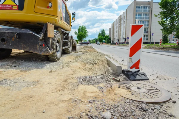 Şehir caddesinde yol işliyor. Kazıcı kovası eski kaldırımı toplayıp bir çöp kamyonuna yüklüyor..