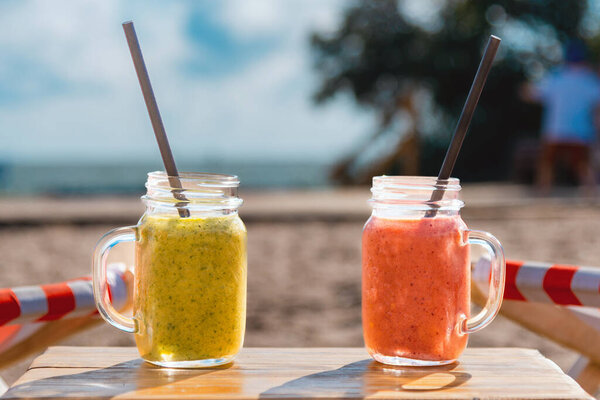 Two fruity cocktails in jar with deep red and green color.cocktails on luxury tropical beach.Blurred sea sky and vacationers background.Summer evening.