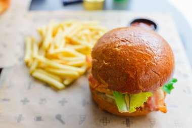 Açık hava restoranında servis edilen lezzetli bir hamburger. Izgara köftenin üstünde peynir, marul, domates ve soğan var. Taze bir bungda servis ediliyor. Seçmeli odak noktası, yakın çekim. Vilnius, Litvanya, 07-21-2023.