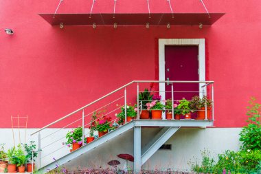 Kırmızı kapısı olan parlak kırmızı bir bina, Litvanya 'nın Vilnius kentindeki kırmızı metal bir duvarın karşısında bitkilerle dolu saksılar..