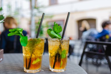 Alkol içeceği. Dışarıdaki Masa Kafe 'de. Alkollü bardaklar ve yarım limonlu, nane yapraklı. Limonlu kokteyl mojito ve nane yaprağı. Şehir hayatı. Kafenin arka planı bulanık. İyi akşamlar..
