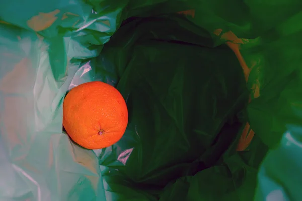 A green garbage bag in the trash. There is an Orange inside.Top view.
