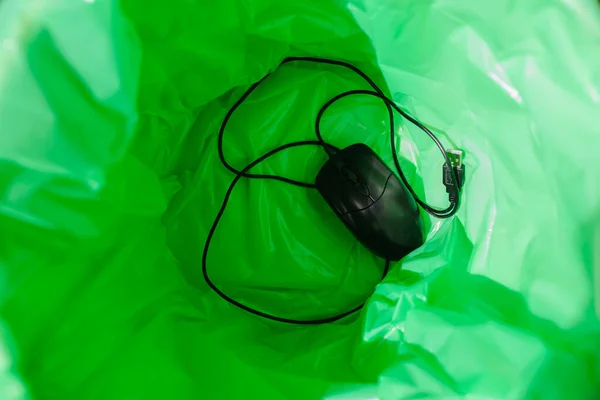 A green garbage bag in the trash. There is a computer mouse inside.Top view.