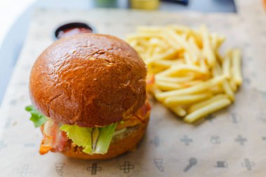 Açık hava restoranında servis edilen lezzetli bir hamburger. Izgara köftenin üstünde peynir, marul, domates ve soğan var. Taze bir bungda servis ediliyor. Seçmeli odak noktası, yakın çekim. Vilnius, Litvanya, 07-21-2023.