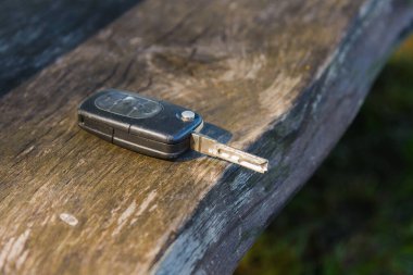 Terk edilmiş, unutulmuş araba anahtarı. Yaz parkındaki bir bankta, ahşap bir tahtanın üzerinde. Seçmeli odak noktası..