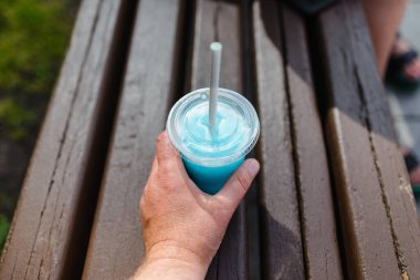 Bir adam yaz şehrinde elinde ferahlatıcı mavi bir içecek tutuyor..