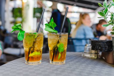 Alkol içeceği. Dışarıdaki Masa Kafe 'de. Alkollü bardaklar ve yarım limonlu, nane yapraklı. Limonlu kokteyl mojito ve nane yaprağı. Şehir hayatı. Kafenin arka planı bulanık. İyi akşamlar..