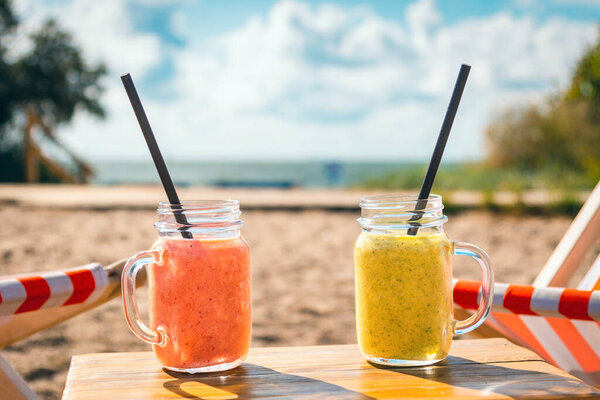 Two fruity cocktails in jar with deep red and green color.cocktails on luxury tropical beach.Blurred sea sky and vacationers background.
