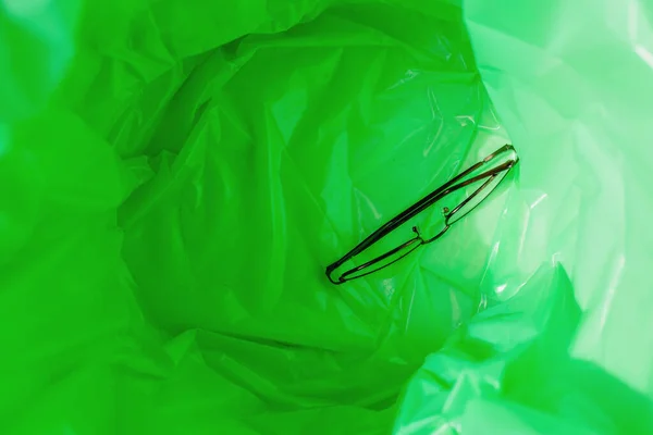 A green garbage bag in the trash. There is an eyeglasses inside.Top view.