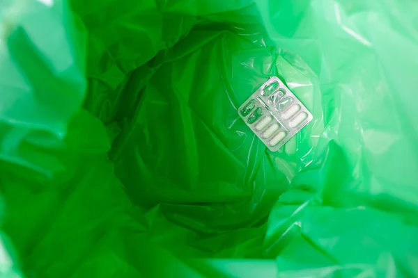 A green garbage bag in the trash. There is a medicines inside.Top view.