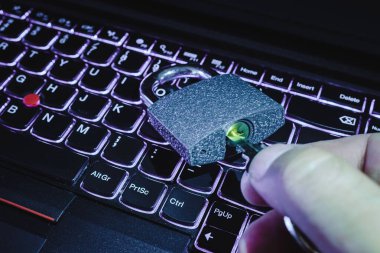 Siber güvenlik soyut kavramı. Bilgisayarın klavyesinde asma kilidi açan adamın eli. Tonlu, yakın plan, klavyeye odaklı..