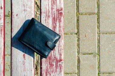 Yazın siyah erkek deri cüzdanı dışarıda, ahşap bir bankta yatıyor..