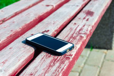 Birisi cep telefonunu parkta bir bankta unutmuş, telefonunu bankta kaybetmiş. Parkta unutulmuş bir akıllı telefon. Bankta duran cep telefonunun yakın çekimi..