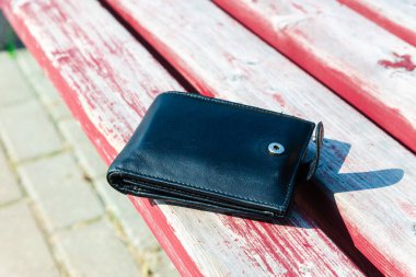 Yazın siyah erkek deri cüzdanı dışarıda, ahşap bir bankta yatıyor..