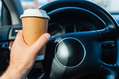 Trafik sıkışıklığında sabah araba kullanırken elinde kağıt bardak sıcak kahve içen bir kişi. Ulaşım ve araç trafiği kavramı.