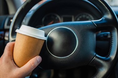 Trafik sıkışıklığında sabah araba kullanırken elinde kağıt bardak sıcak kahve içen bir kişi. Ulaşım ve araç trafiği kavramı.