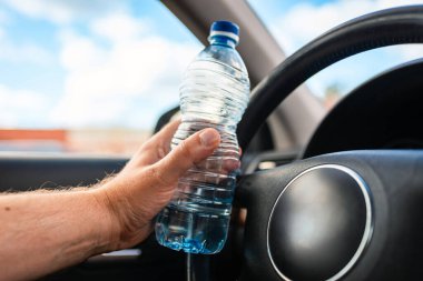 Trafikte araba kullanırken elinde plastik su şişesi olan bir erkek. Yaklaş..