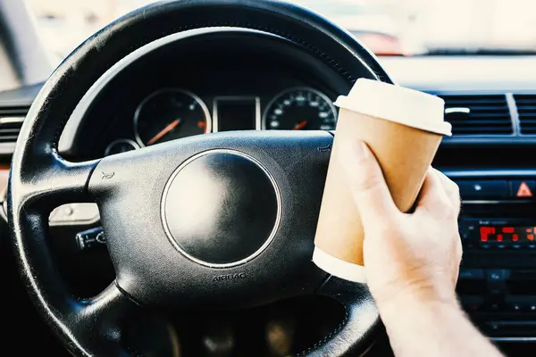 Man holding coffee paper cup in car.A person drinking paper cup hot coffee in hand while driving in a car in the traffic jam morning.Transportation and vehicle traffic jam concept.